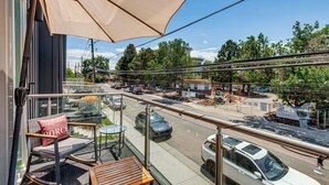 A balcony with a chair, table, and umbrella, overlooking a street with cars and construction.