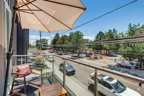 Een balkon met een stoel, tafel en parasol, met uitzicht op een straat met auto's en bouwactiviteiten.