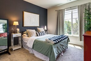 Een slaapkamer met een bed, nachtkastjes, een lamp, een spiegel, een raam met gordijnen en een plant.