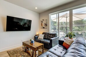 Een moderne woonkamer met een leren bank, een flatscreen televisie, een salontafel en een groot raam met balkonzicht.