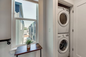 Un cuarto de lavado con ventana, una planta en maceta y dos lavadoras apiladas.