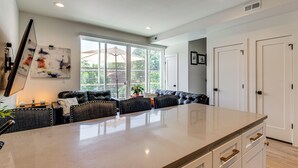A spacious kitchen with a large island, dark leather seating, and a view of the outdoors through large windows.
