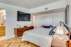 Ein modernes Schlafzimmer mit einem großen Bett, einem Fernseher, einer Holzkommode, einem Schreibtisch und einer Lampe.