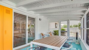 A covered outdoor dining area with a wooden table and metal chairs, a yellow locker, and a glass door leading outside. - Stylish MCM Retreat: 27 Days or More (Palm Desert)