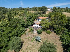 Eine weiße Villa mit rotem Ziegeldach, umgeben von dichtem Grün und Bäumen, auf einer Hügelkuppe.