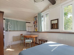 Ein Schlafzimmer mit einem Bett, einem Sessel, einem kleinen Tisch, einem Bücherregal und einem Fenster.