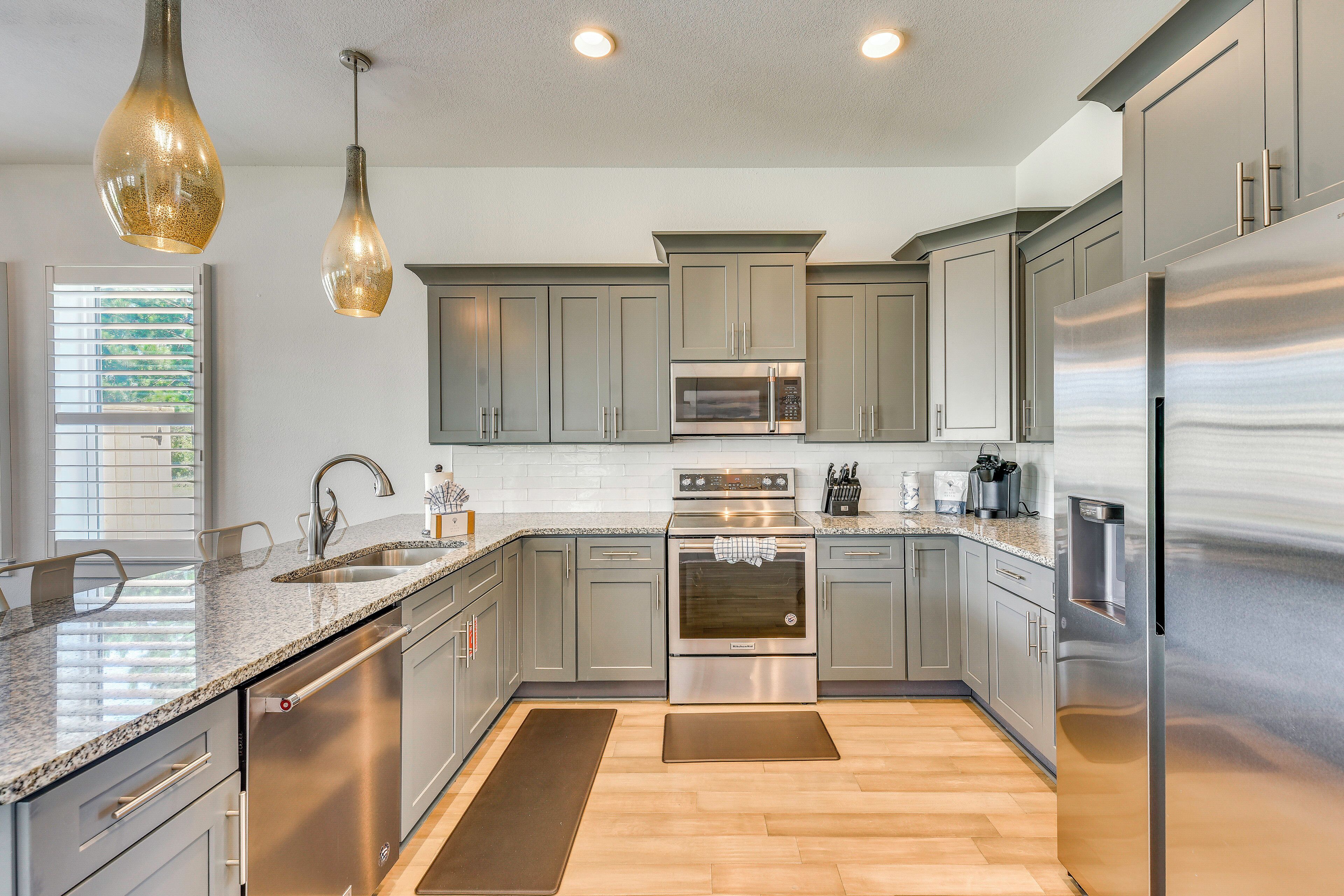 A modern kitchen with stainless steel appliances, grey cabinets, and pendant lighting.
