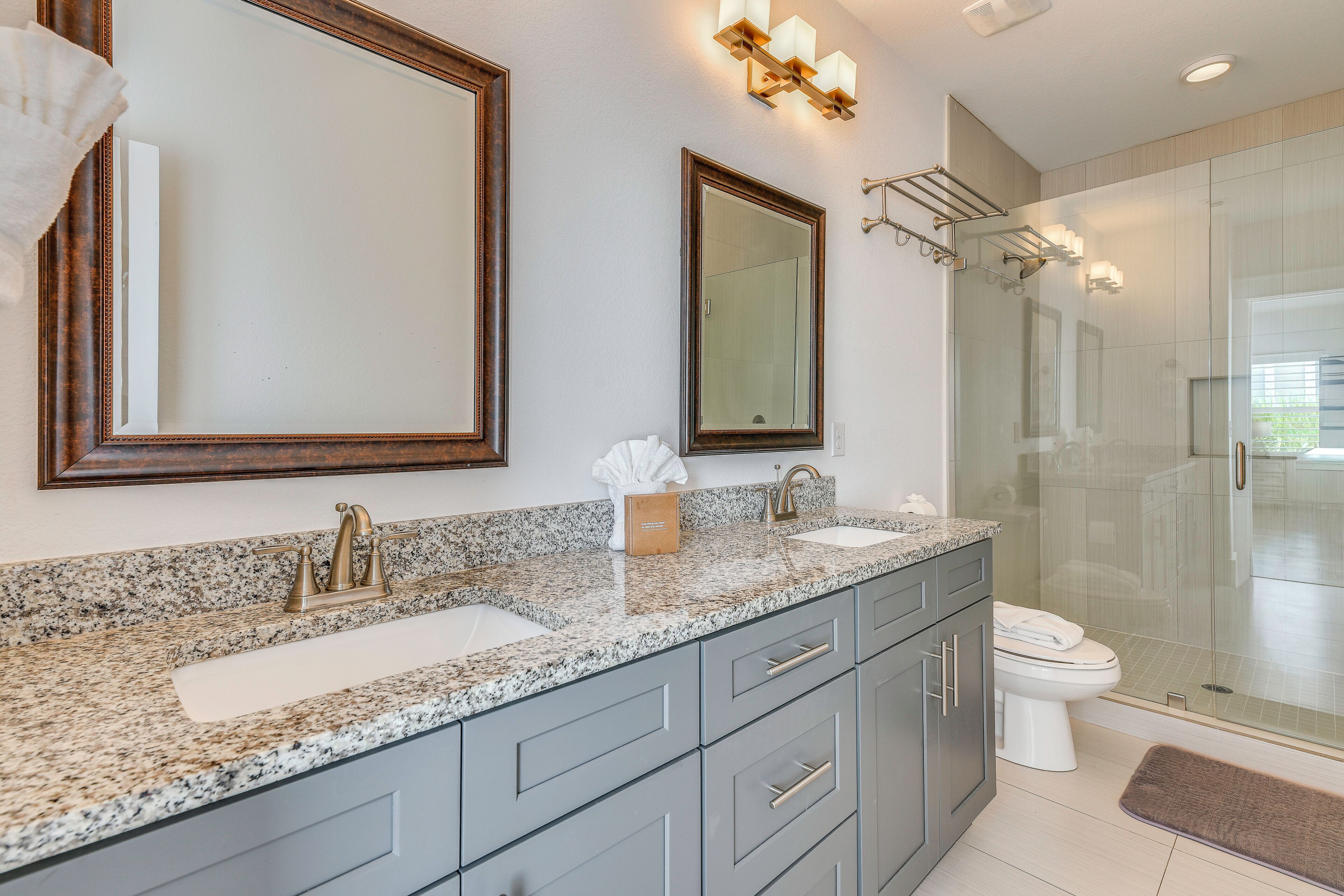 A modern bathroom with a granite countertop, two sinks, a toilet, and a glass shower enclosure.
