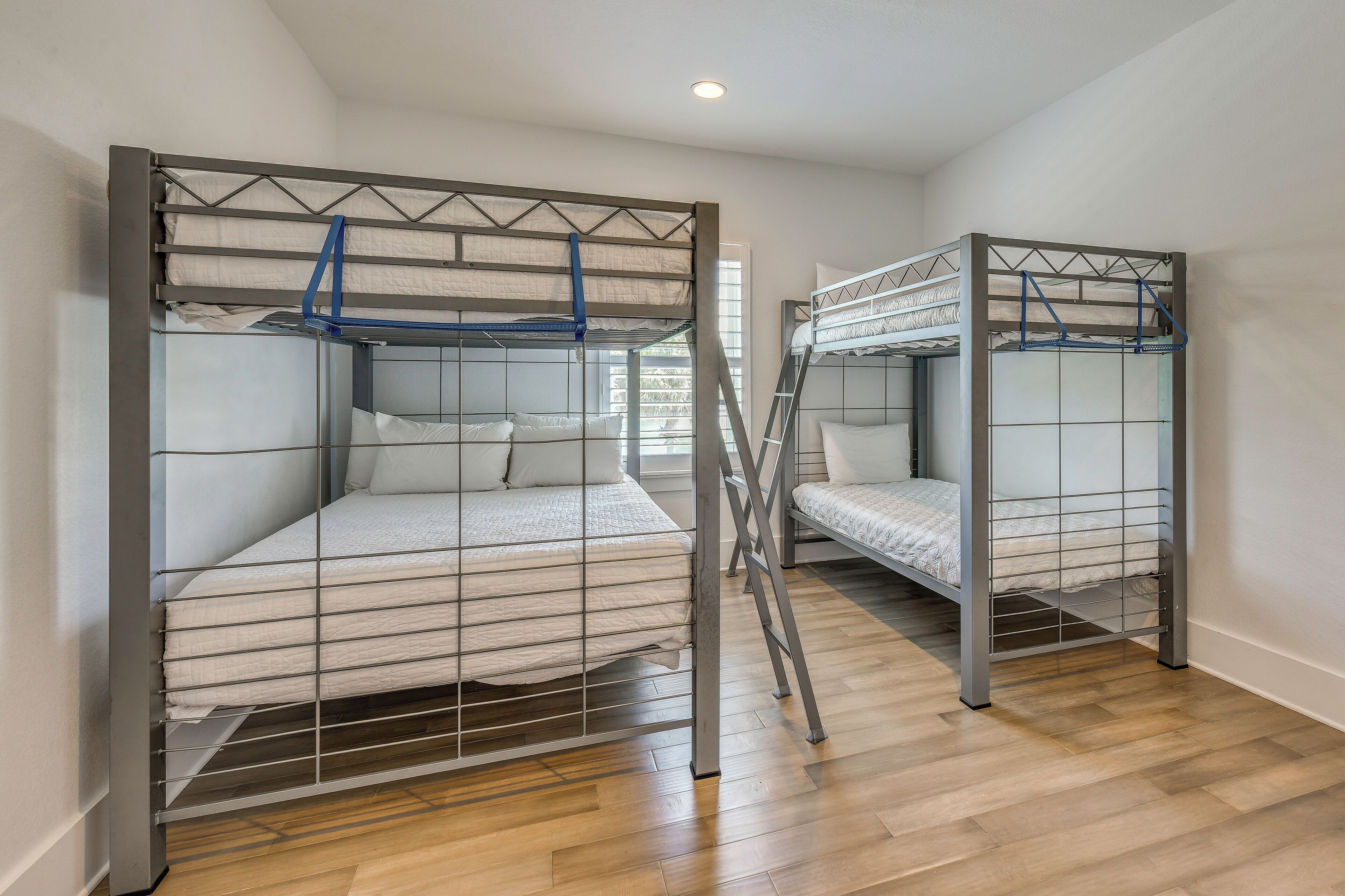 Two bunk beds with metal frames and white bedding, a wooden floor, and a window with natural light.