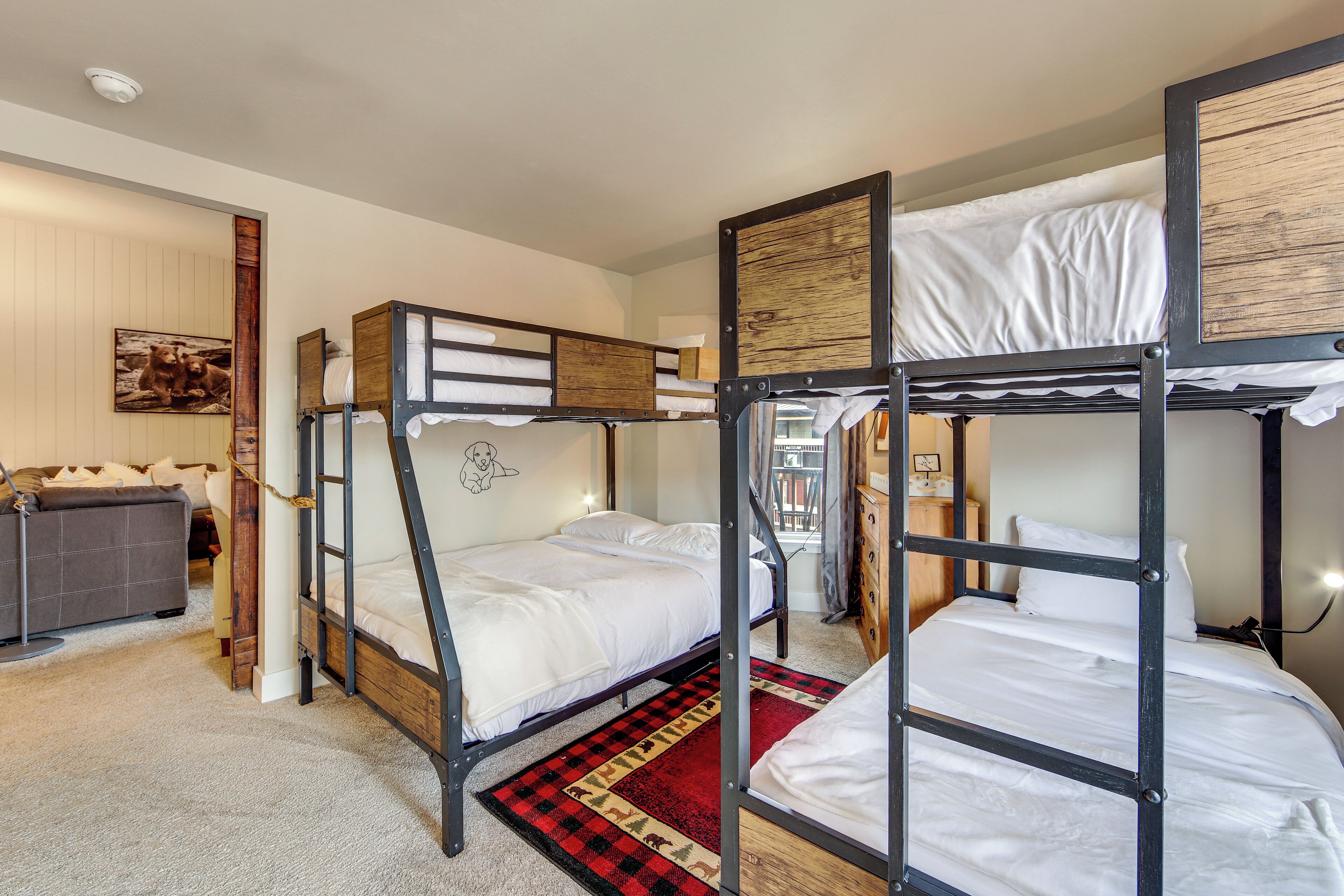 Habitación con literas, un tapete rojo y negro a cuadros, un sofá gris y un marco de madera en la pared.