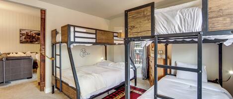 Habitación con literas, un tapete rojo y negro a cuadros, un sofá gris y un marco de madera en la pared.