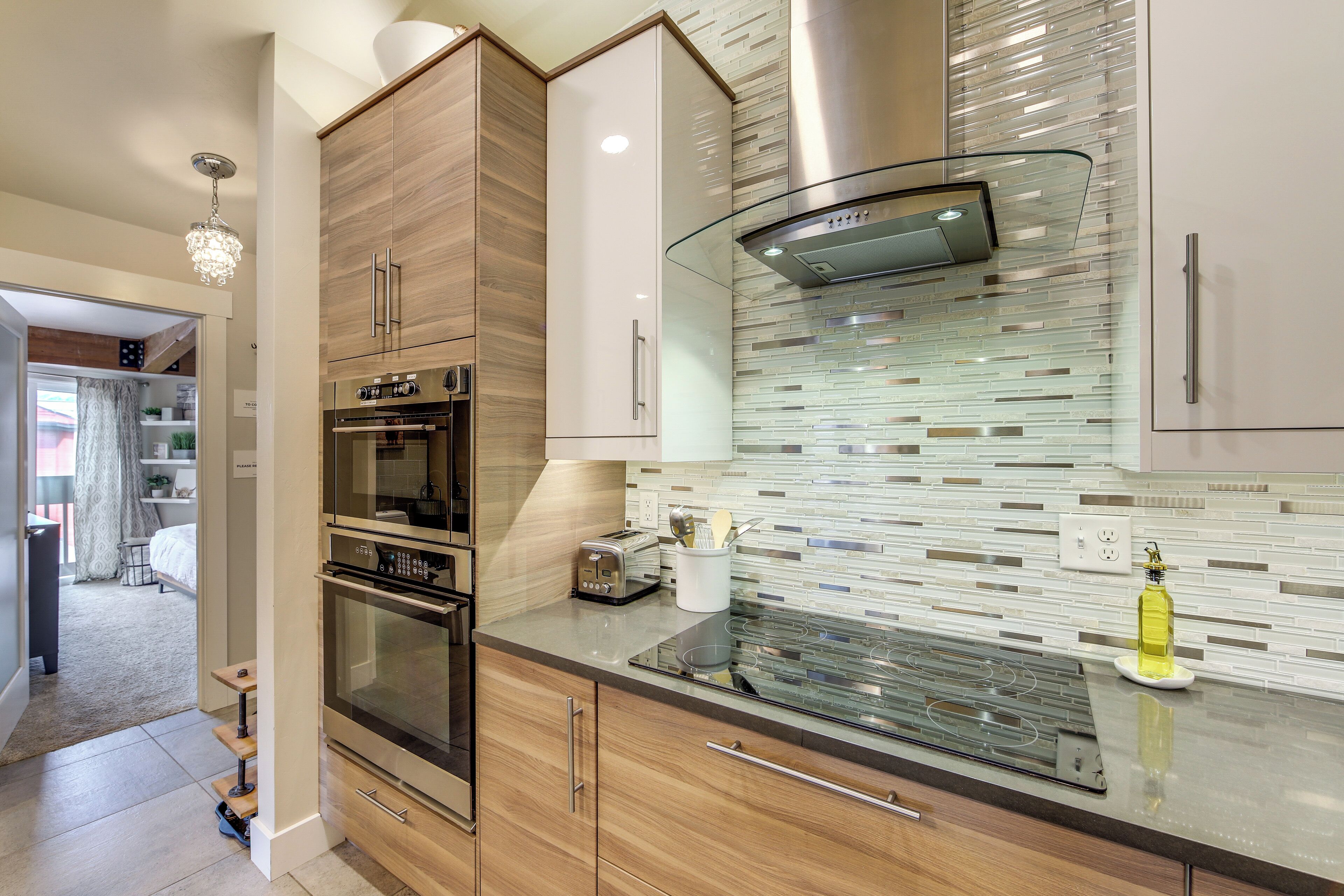 A modern kitchen with wooden cabinets, a built-in oven, a glass cooktop, and a stainless steel range hood.