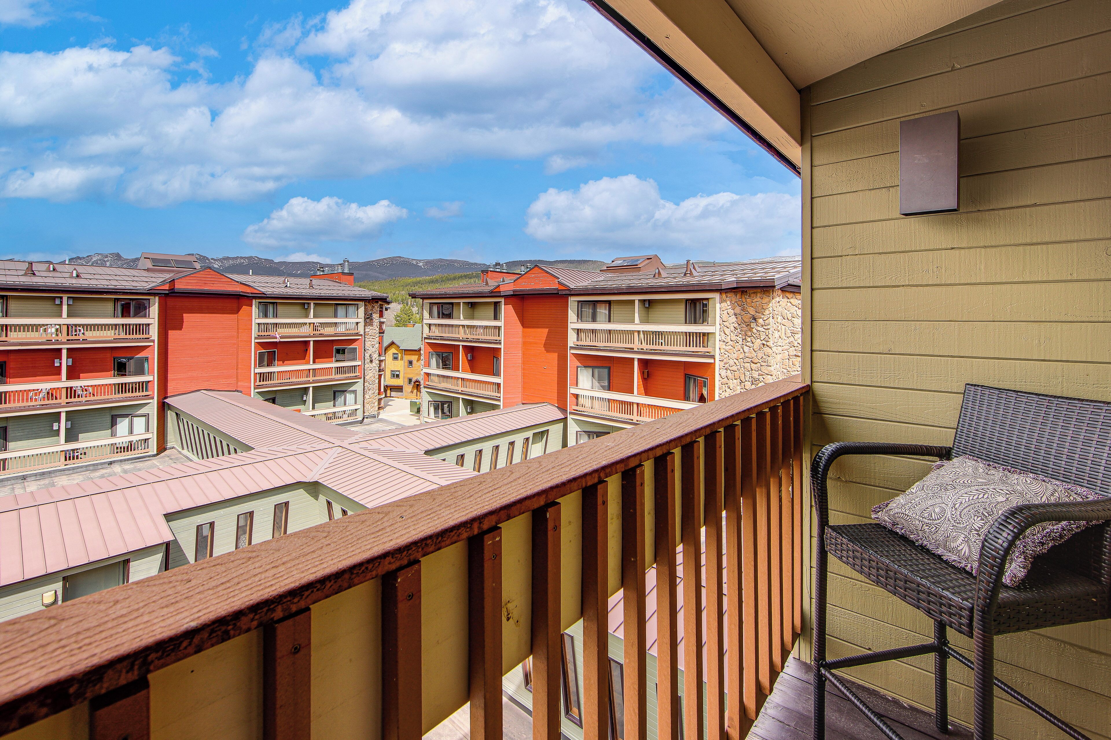 A balcony with a wicker chair and a view of multi-story buildings with balconies.