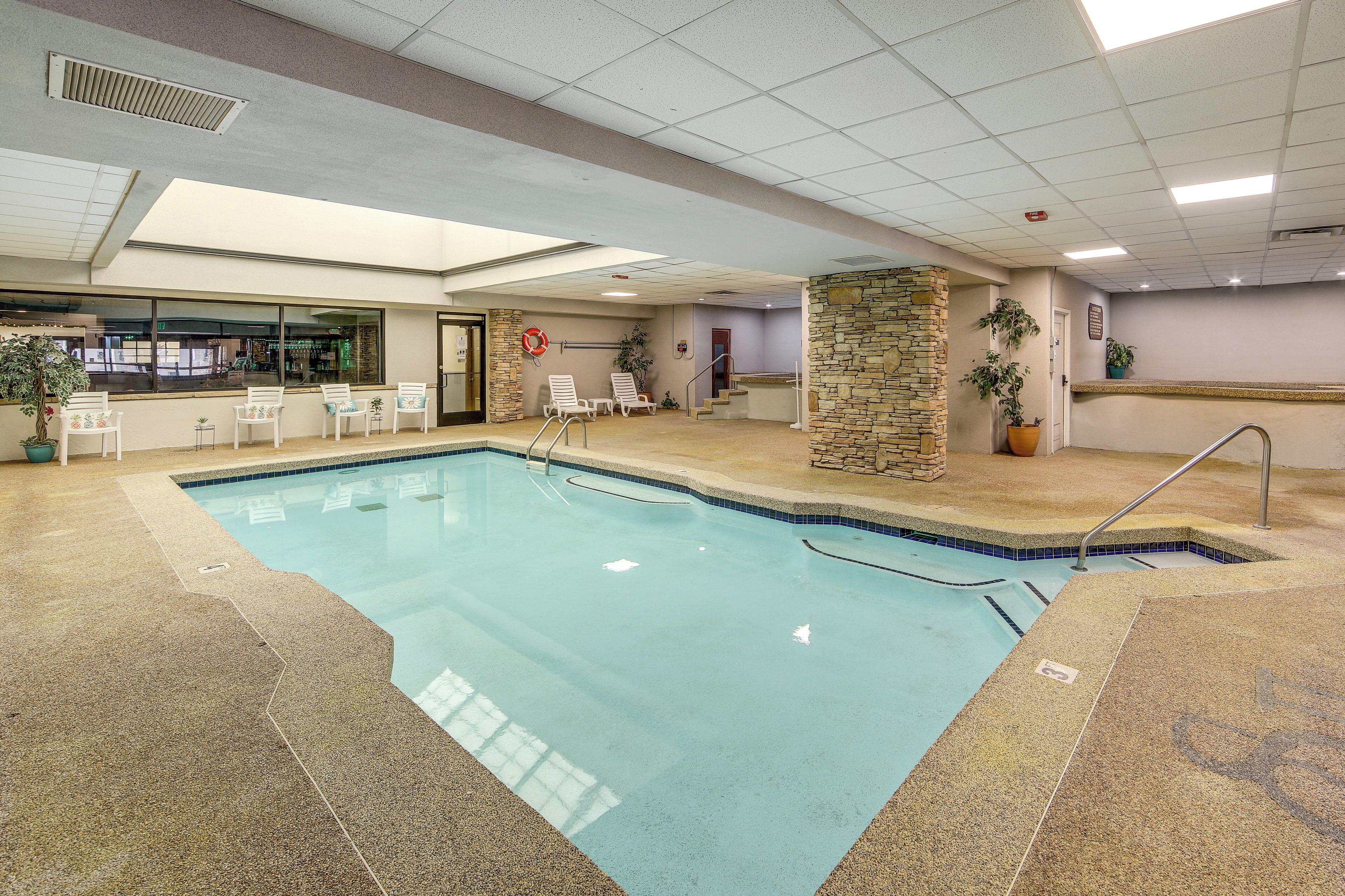 Ein Hallenbad mit Steinwand, Liegestühlen und Blick ins Freie.