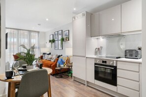 A modern kitchen with a built-in oven, a toaster, and a dining area with a table and chairs. - Luxury Liverpool Waterfront Apartment (Merseyside)