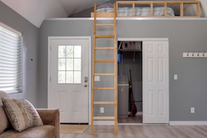 A loft bedroom with a wooden ladder, a bunk bed, a closet, and a door.