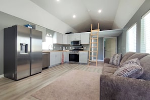 A modern kitchen with stainless steel appliances, a wooden ladder, and a grey couch with patterned cushions. - Whale Watch, Fish & Hike Glaciers! Homer Apartment (Homer)