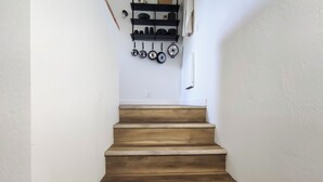 Una escalera de madera que conduce a una zona de cocina con ollas y sartenes colgadas en la pared.