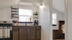 Una cocina con armarios de madera, estufa, cafetera y una ventana con persianas.
