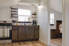 A kitchen with wooden cabinets, a stove, a coffee maker, and a window with blinds.