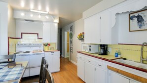 A compact kitchen with white cabinets, a microwave, and a stove. There is a dining table with chairs. - Hike, Golf & Fish! Pet-friendly Getaway in Ashton (Ashton)
