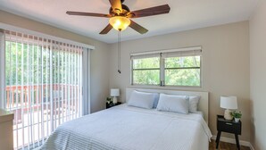 A bedroom with a bed, a ceiling fan, a window, and a nightstand with a lamp.