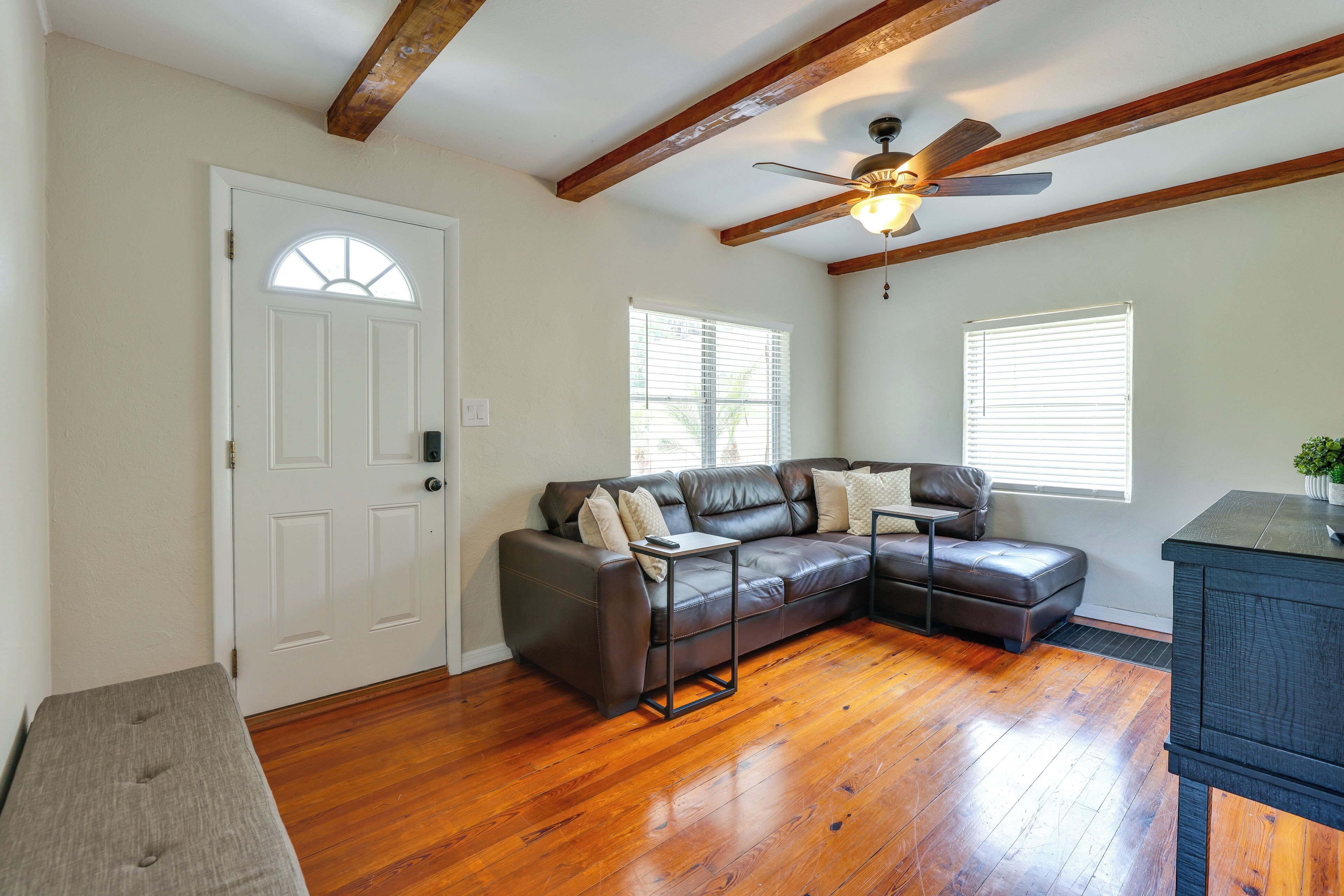 A living room with a sectional sofa, wooden flooring, a ceiling fan, and a door with a window.
