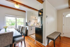 Una cocina con armarios blancos, un refrigerador negro, vigas de madera y un comedor con mesa y sillas.