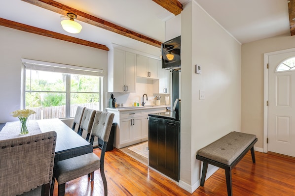 A kitchen with white cabinets, a black refrigerator, wooden beams, and a dining area with a table and chairs.