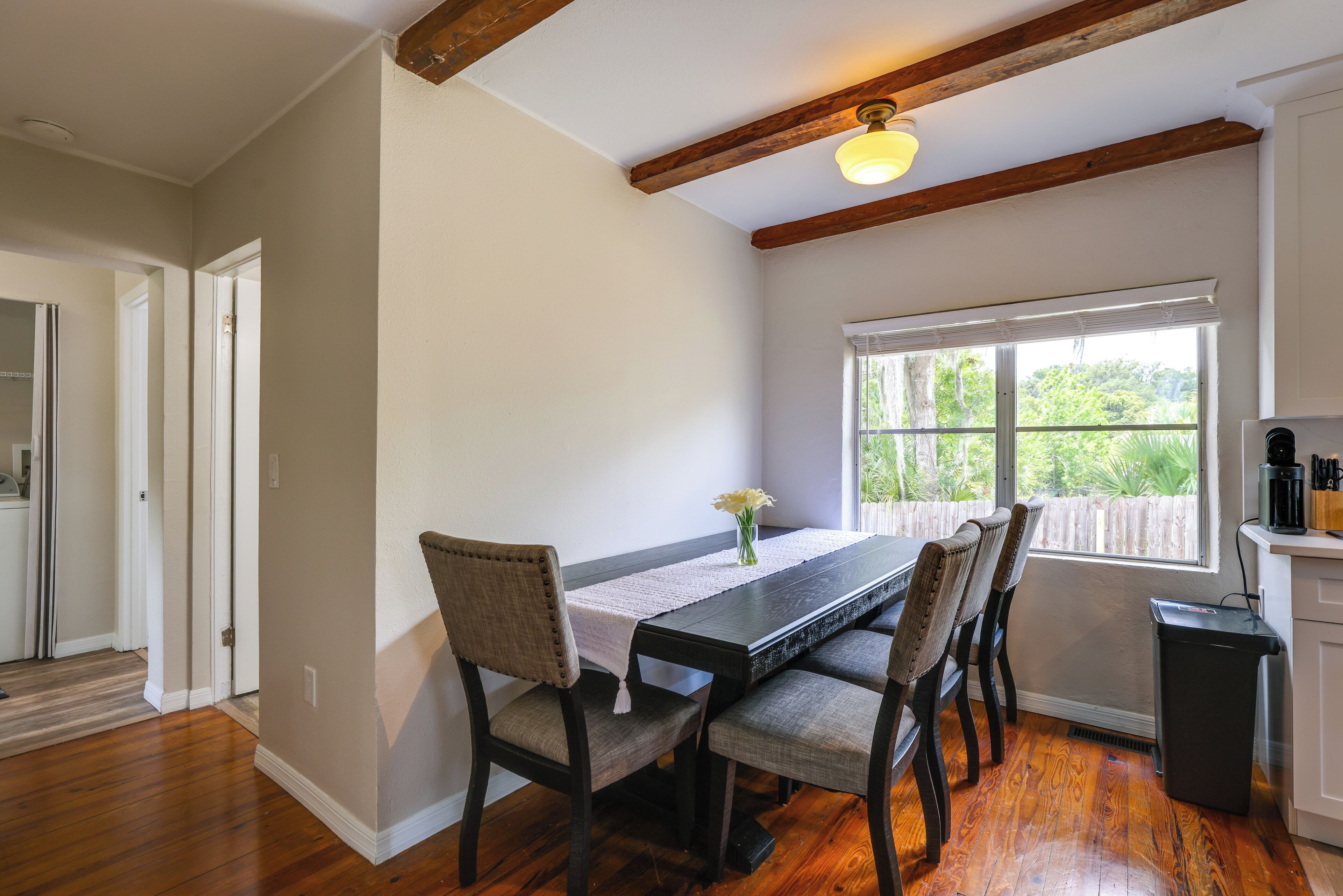 A dining area with a wooden table, chairs, a window with a view, and a ceiling light fixture.