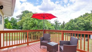 A wooden deck with wicker chairs and a red umbrella.