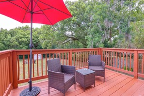 Una terraza de madera con mobiliario de mimbre y un paraguas rojo.