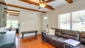 A living room with a brown leather sofa, a small table, a ceiling fan, wooden beams, and a window with blinds.