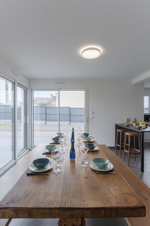 Ein Essbereich mit einem langen Holztisch, gedeckt für sechs Personen, großen Fenstern und Blick auf die Stadt.