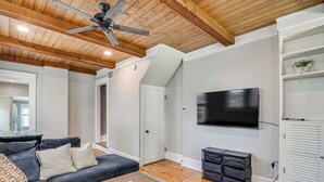 Una sala de estar con ventilador de techo, televisor de pantalla plana, sofá, mesa de centro y mueble de almacenamiento.