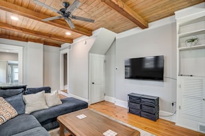 A living room with a ceiling fan, a flat-screen TV, a sofa, a coffee table, and a storage unit.