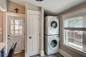 A laundry room with a double washer and dryer, a white door, and a window with blinds.