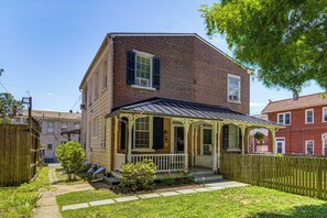 A two-story brick house with a porch, a fenced yard, and a small tree.