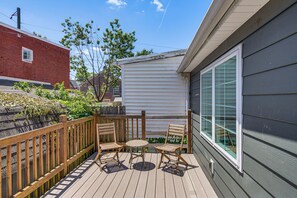 A deck with wooden chairs and a table, a brick building, and a white house in the background.