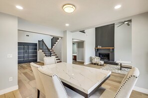 Ein modernes Wohnzimmer mit einem Esstisch aus Marmor, weißen Polsterstühlen, einem Kamin und einer Treppe.