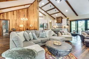 A spacious living room with a large sectional sofa, a round coffee table, and a dining area with a kitchen in the background. - Roxboro Lake Family Retreat and Spa (Prospect Hill)