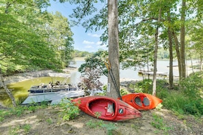 A serene lakeside setting with a boat docked near a tree, a red kayak, and a small dock extending into the water. - Roxboro Lake Family Retreat and Spa (Prospect Hill)