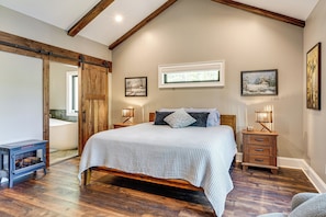 A bedroom with a wooden bed, a wooden nightstand with a lamp, a large window, and a sliding door. - Roxboro Lake Family Retreat and Spa (Prospect Hill)