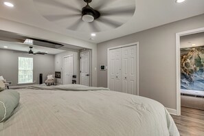 A bedroom with a large bed, two white doors, a ceiling fan, and a window with blinds.