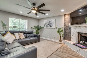 A living room with a gray leather sofa, a ceiling fan, a fireplace, and a large window.