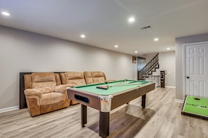 A pool table with a cue ball and rack of balls, a brown sofa, and a staircase leading to an upper level. - Pool, Hot Tub & Game Room! Stockbridge Oasis (Stockbridge)