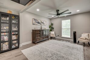 A spacious room with a large wooden cabinet, a ceiling fan, a large window with blinds, and a white rug. - Pool, Hot Tub & Game Room! Stockbridge Oasis (Stockbridge)