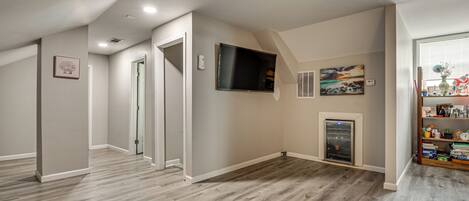 A spacious room with a wooden floor, a flat-screen TV mounted on the wall, and a fireplace.