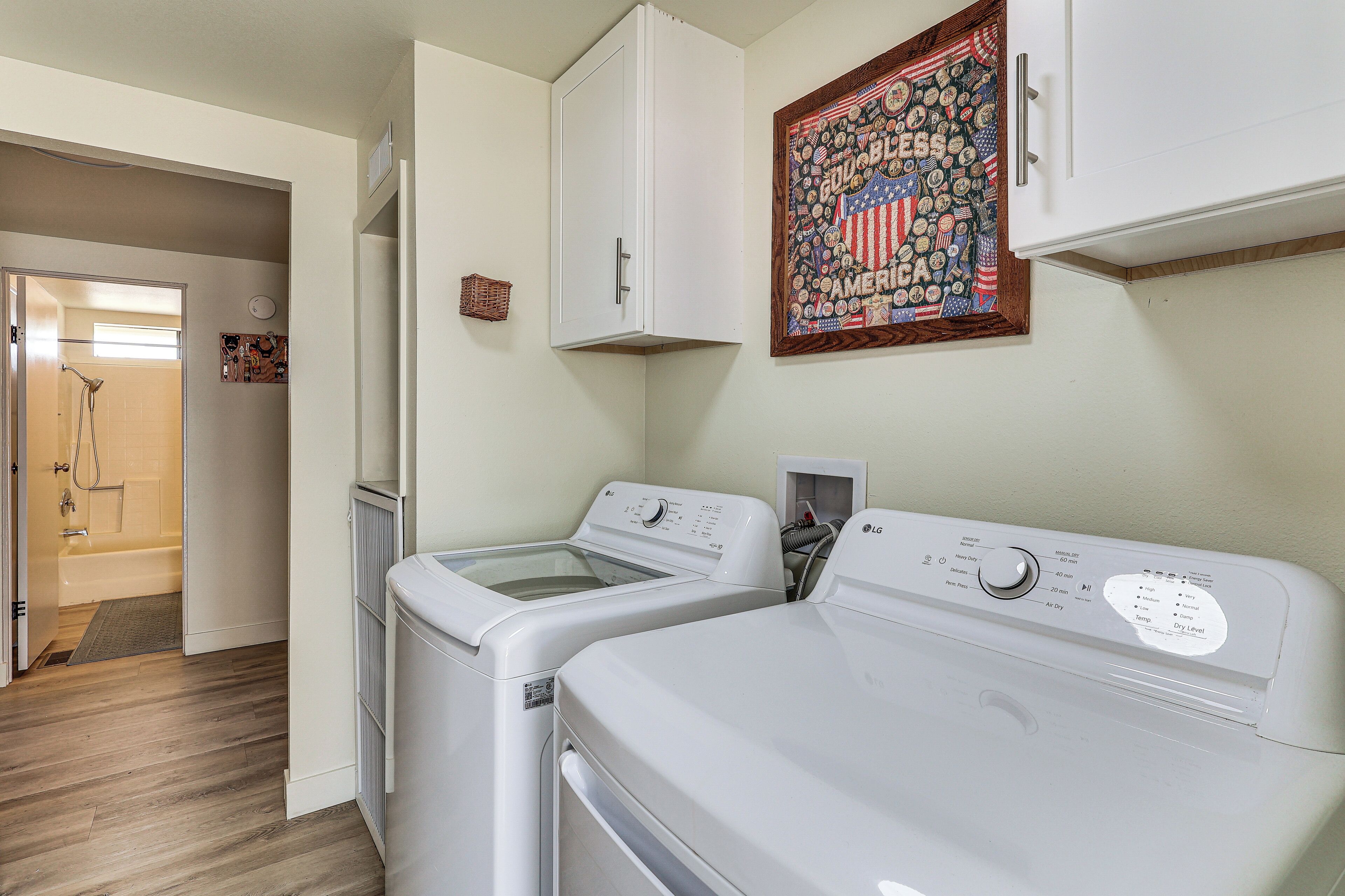 A laundry room with two front-loading washers and dryers, a wooden floor, and a wall-mounted American flag decoration.