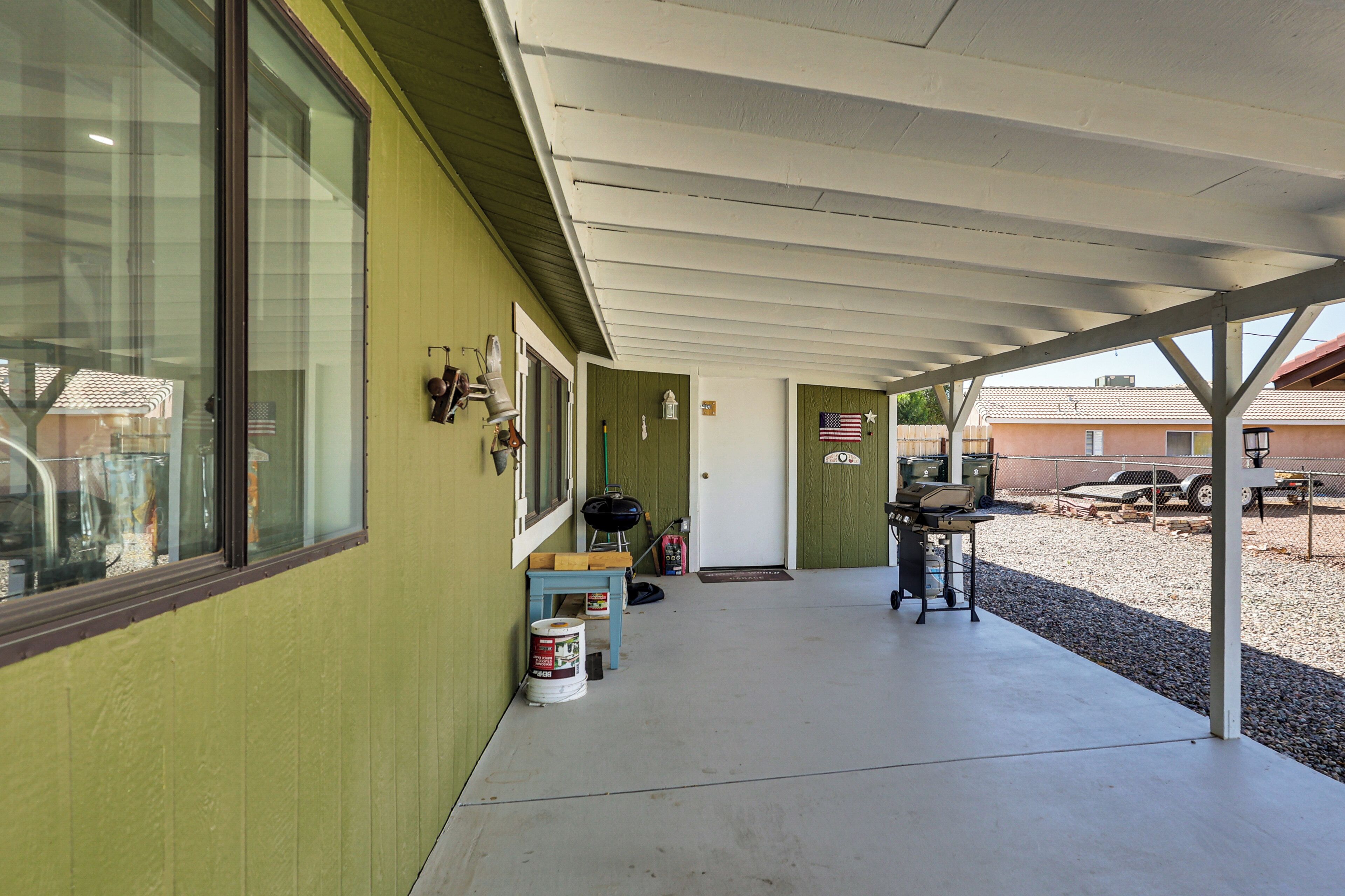 A covered outdoor area with a concrete floor, a grill, and a table with chairs.